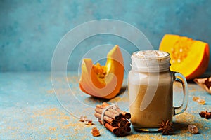 Pumpkin spiced latte or coffee in glass on turquoise vintage table. Autumn, fall or winter hot drink. Cozy breakfast or snack.