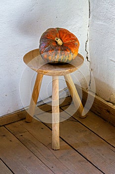 A pumpkin on a three-legged wooden stool.