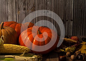 Pumpkins, corn, apples, walnuts and chestnuts, autumn leaves on a wooden background.