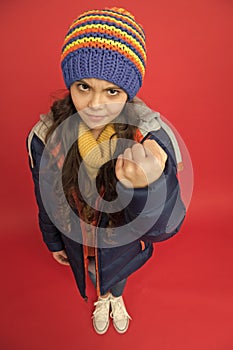 Punch in face. Threatening fist. Little girl wear winter clothes red background. Childhood concept. Emotional girl long