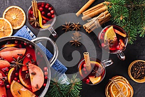 Punch or hot wine in a glass and mulled wine in a cooking pot with spices and fruits on a black textured background