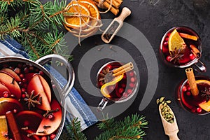 Punch or hot wine in a glass and mulled wine in cooking pot with spices and fruits on a black textured background, top view.