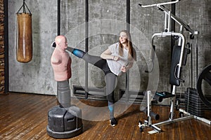 Punching bag bob dummy in gym, young woman kicks.