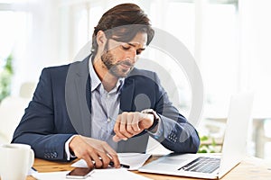 Punctuality is crucial in this office. A handsome businessman checking the time on his watch at his desk.