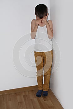 Punished for a bad deed, the boy stands in the corner, shame covers his face with his hands, pedagogical concept photo