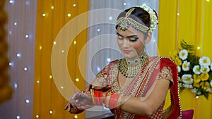 Punjabi bride putting on golden bridal bangles with Chuda in Henna decorated hands