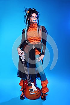 Punk rock girl guitarist posing over blue studio background. Trendy model with hairstyle.