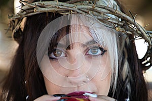 Punky girl with blonde and brunette hair holding a red apple in her hands, the girl wears a crown of thorns like christ on her