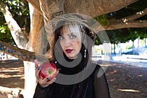 Punky girl with blonde and brunette hair holding a red apple in her hands, the girl wears a crown of thorns like christ on her