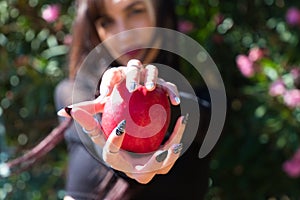 Punky girl with blonde and brunette hair holds a red apple in her hands and stares at it. The girl is a witch from the fairy tale