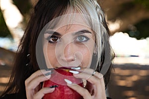 Punky girl with blonde and brunette hair holds a red apple in her hands and stares at it. The girl is a witch from the fairy tale