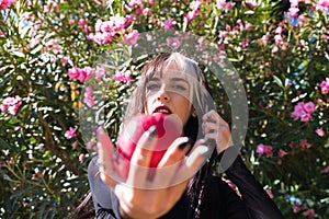 Punky girl with blonde and brunette hair holds a red apple in her hands and stares at it. The girl is a witch from the fairy tale