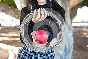 Punky girl holding a red apple and a crown of thorns in her hands. represents the apocalypse from the beginning with adam and eve
