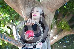 Punky girl holding a red apple and a crown of thorns in her hands. represents the apocalypse from the beginning with adam and eve