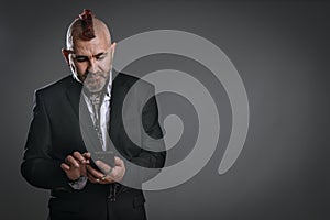 punky-style man dressed in jacket suit looks at his phone in studio shot