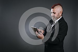 punky-style man looks at his tablet dressed in business suit in camera shot