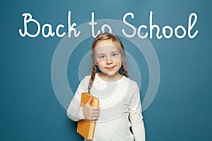 Pupil with braids holding yellow book on blue background. Back to school and childhood concept