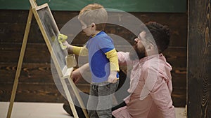 Pupil drawing on chalkboard. Teacher controls learning process. Father teaching son. Pupil with teacher at school. Side