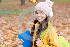 Pupil in earpieces hold book while walking in park, education photo