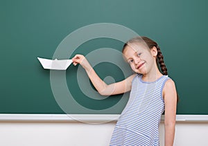 Pupil with origami ship posing at school board, empty space, education concept