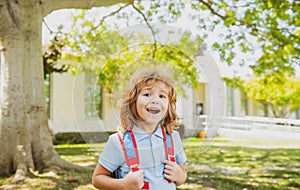 Pupil of primary school with book in hand near school park. Schoolboy with backpack near building outdoors. Beginning of