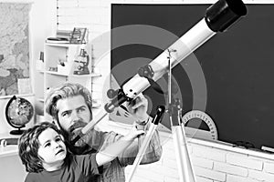Pupil watching stars with a teacher. Astronomy telescope. Happy cute industrious child is sitting at a desk indoors