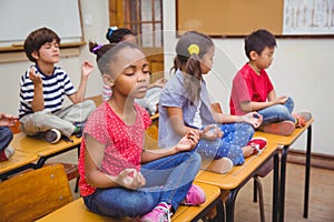 Pupils meditating in lotus position on desk in classroom