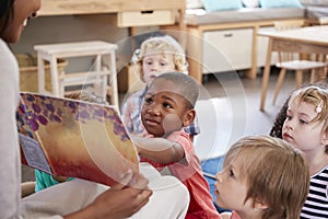 Pupils At Montessori School Looking At Book With Teacher