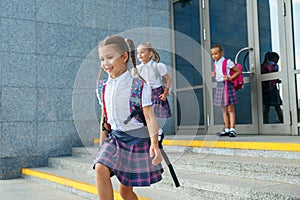 Pupils of primary school. Girls with backpacks near building outdoors. Beginning of lessons. First day of fall.