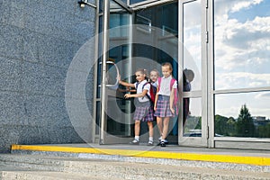 Pupils of primary school. Girls with backpacks near building outdoors. Beginning of lessons. First day of fall.