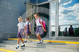 Pupils of primary school. Girls with backpacks near building outdoors. Beginning of lessons. First day of fall.