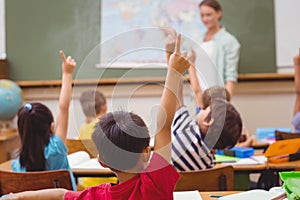 Pupils raising hand during geography lesson in classroom