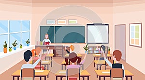 Pupils raising hands to answer question teacher sitting desk education concept modern school classroom interior chalk