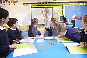 Pupils Sitting At Table As Teacher Stands By Whiteboard