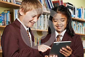 Pupils Wearing School Uniform Using Digital Tablet In Library