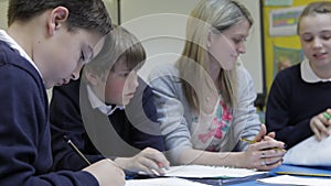 Pupils Working At Table With Teacher Helping Them