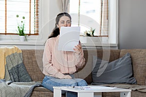 Purchase of real estate. Young caucasian woman sitting on sofa and reading documents bulging eyes. Concept of leasing