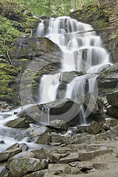 Pure and cold mountain river is running between rocky stones and flows into waterfall