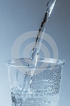 Pure fresh water is pouring into glass or plastic cup in drops close up, healthy drink