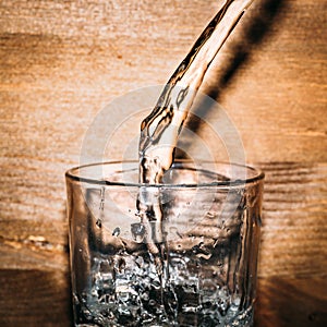 Pure fresh water is pouring into glass on wooden background close up, healthy drink