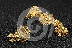Pure gold nuggets from the mine on black sand. Gold ore