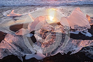 Pure Ice Shining on Black Volcanic Sand at Sunset. Icebergs from Glacier in Sun Rays. Clear Ice in Ocean Waves. Famous