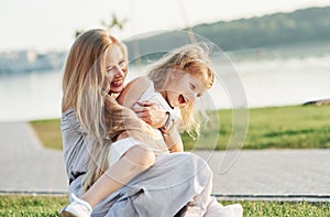 Pure love. Photo of young mother and her daughter having good time on the green grass with lake at background