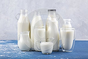 Pure milk drinks in clear jars and bottles are naturally healthy foods placed  on a blue background. A bottle of milk and glass of