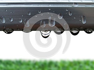 pure water drop on gray aluminum clothes line with blurry green grass lawn