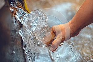 Pure water from the spring is collected in a glass bottle. Transparent cold water from a natural spring pours into a