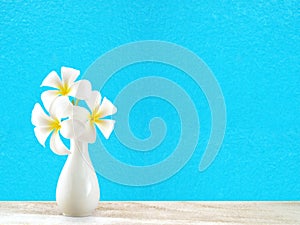 Pure white plumeria bouquet in simple pottery vase on desk floor and pastel blue painted concrete wall with copy space