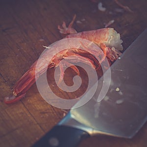 Purified boiled shrimp and a kitchen knife lie on a cutting board. Toned image