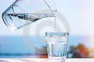 Purified water is poured from a glass jug into a glass