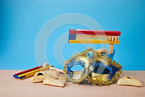 Purim celebration concept with hamantashen cookies, Purim mask and toy noisemaker on blue background